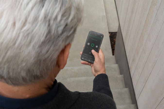 An individual using a smartphone app to control home security settings, viewed from behind as they stand on a concrete staircase.