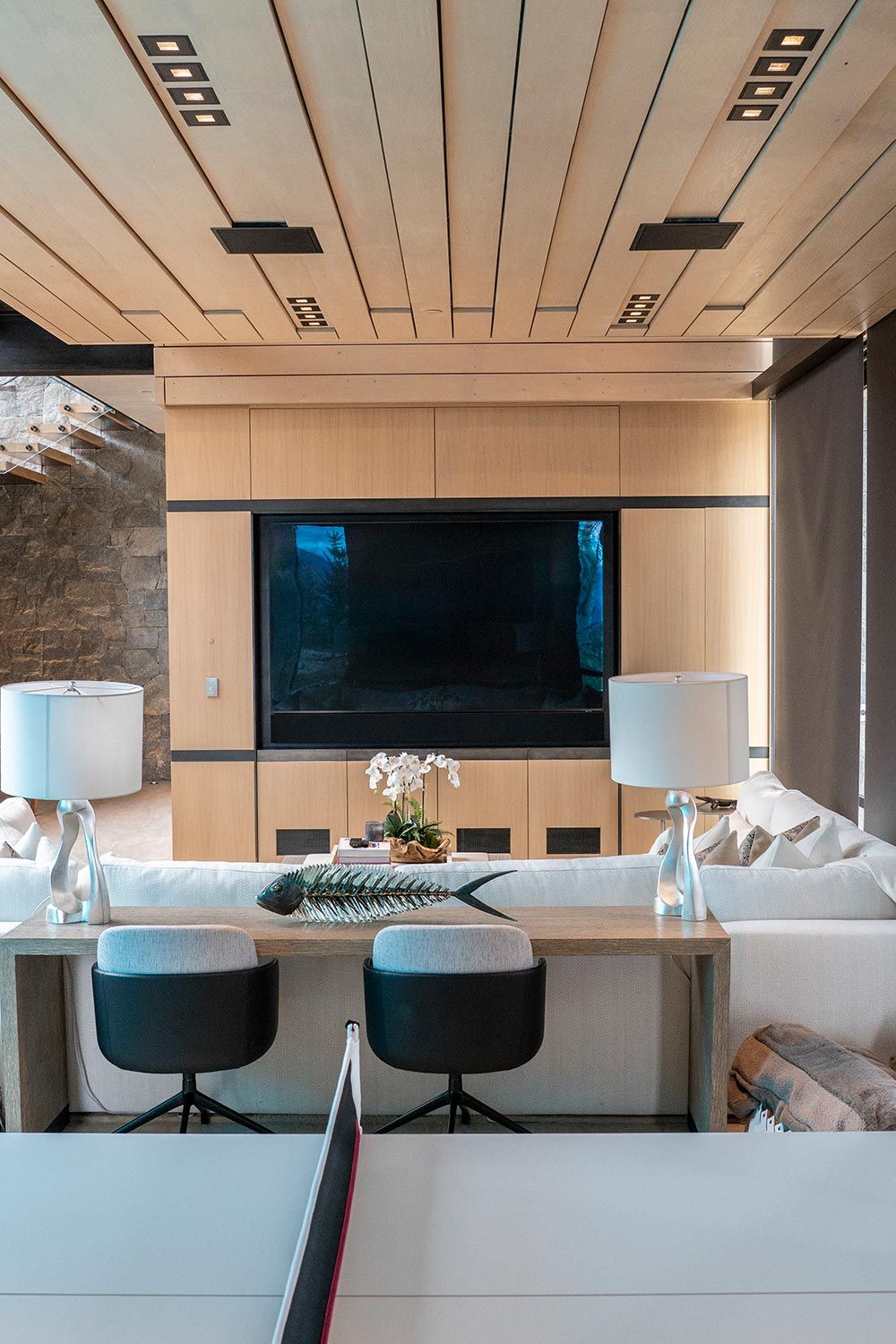 Contemporary living room with wood paneling, a large television, and two silver lamps