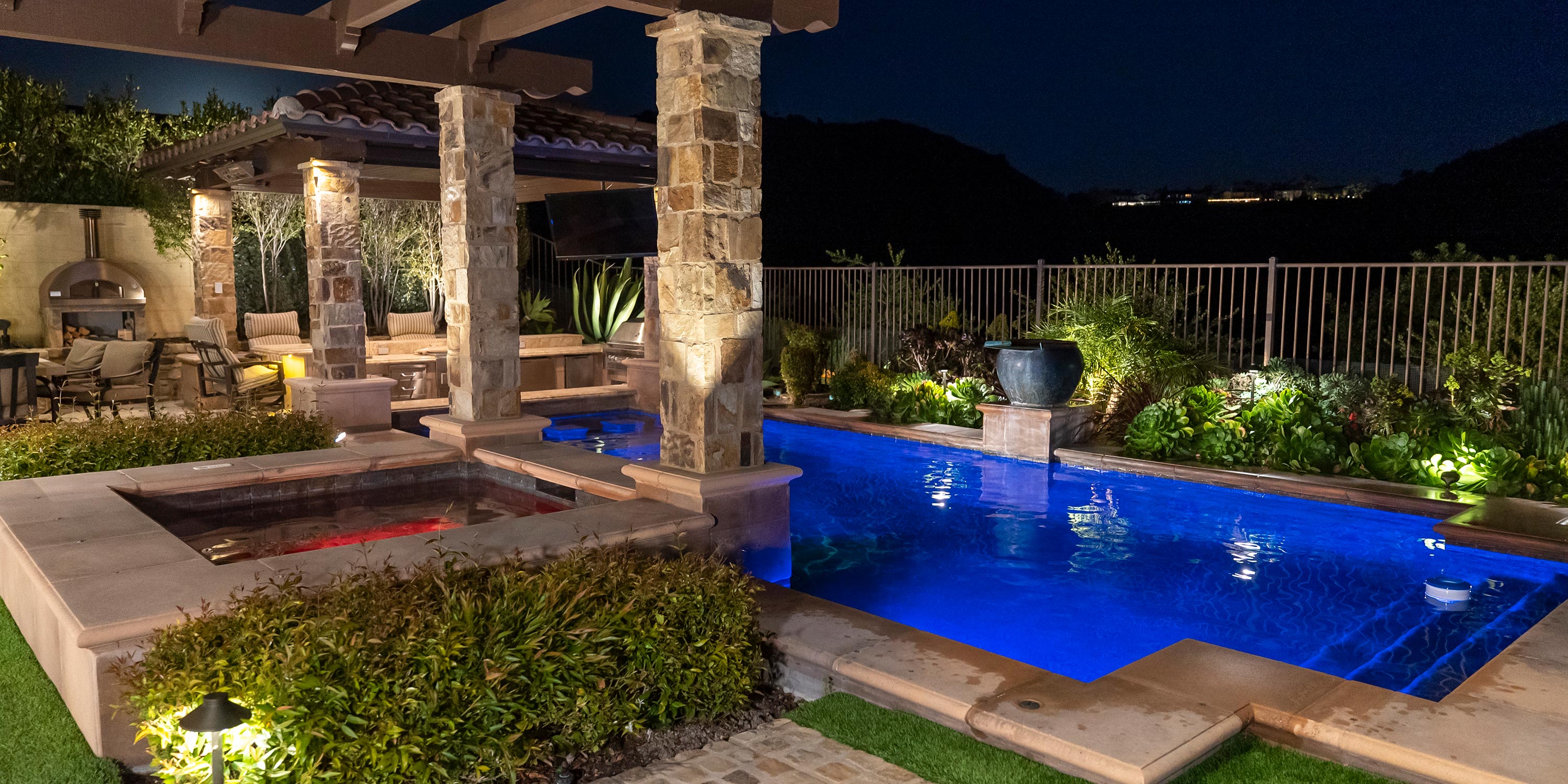 Outdoor living space at night with pool, hot tub, and covered seating area