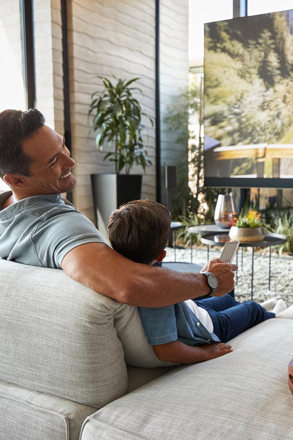 Father and son relaxing on an indoor sofa holding a remote