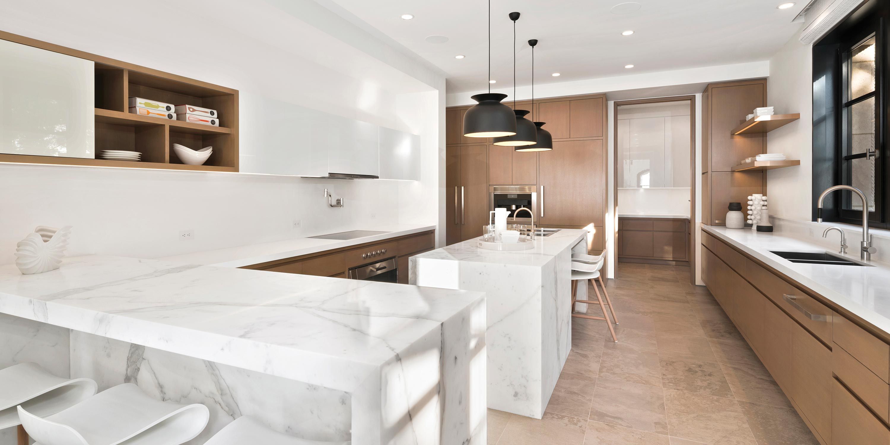 A modern kitchen featuring white marble countertops, sleek wooden cabinetry, and pendant lighting over a central island.