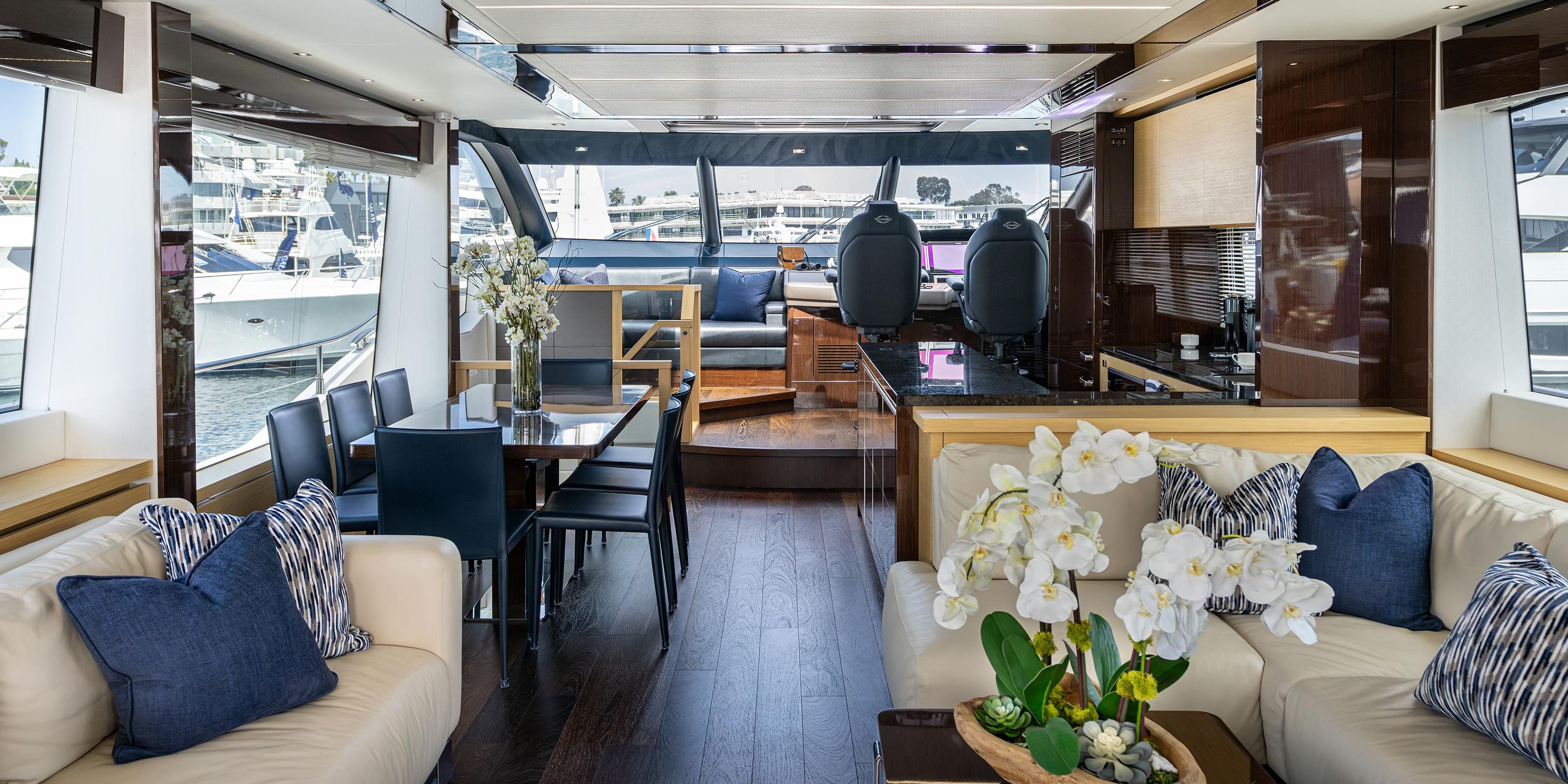 Luxurious yacht main salon with comfortable seating, large windows, and a dining area overlooking the marina.