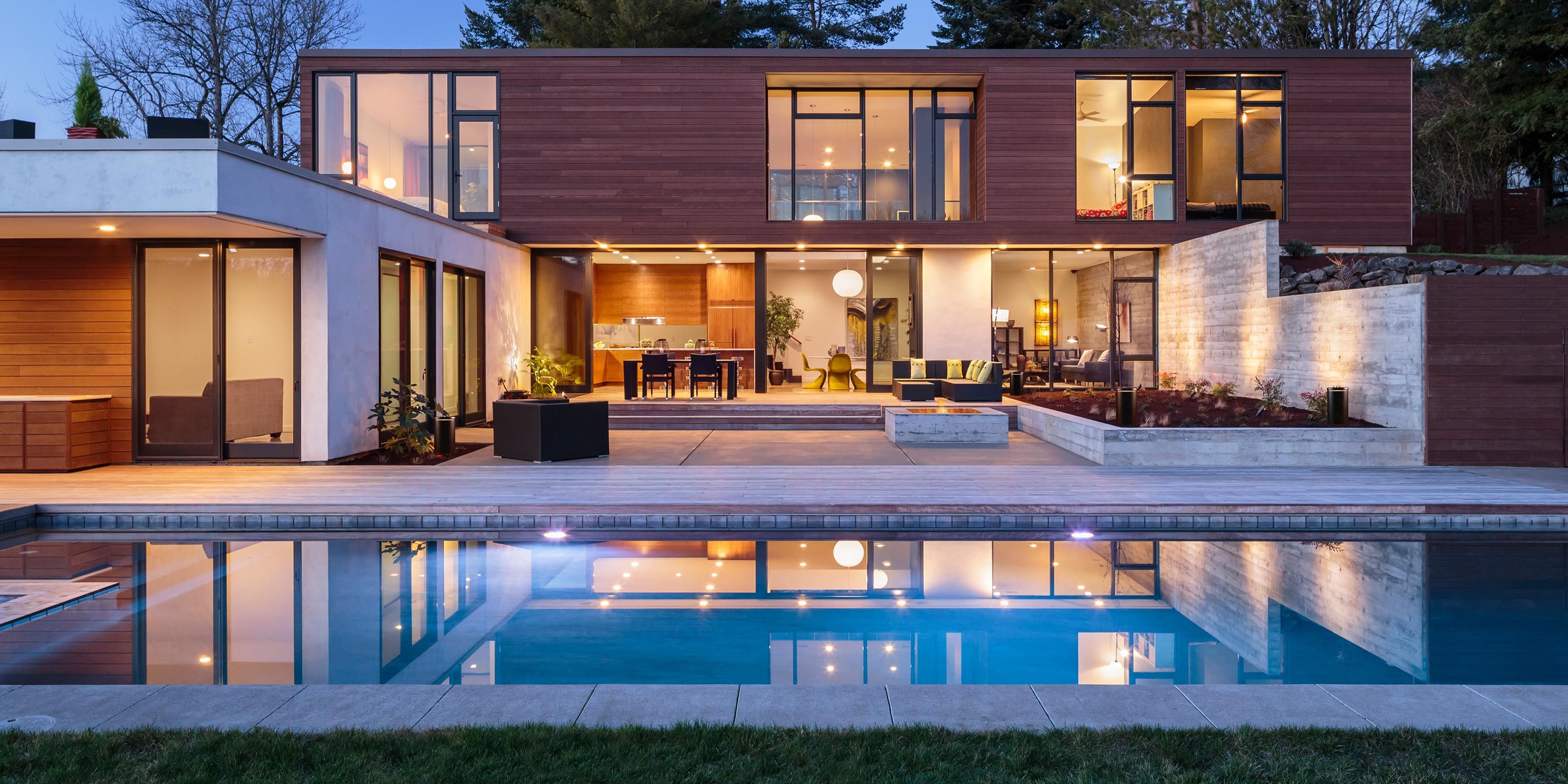 Luxury backyard with an illuminated pool, surrounded by greenery and comfortable lounge chairs for relaxation.